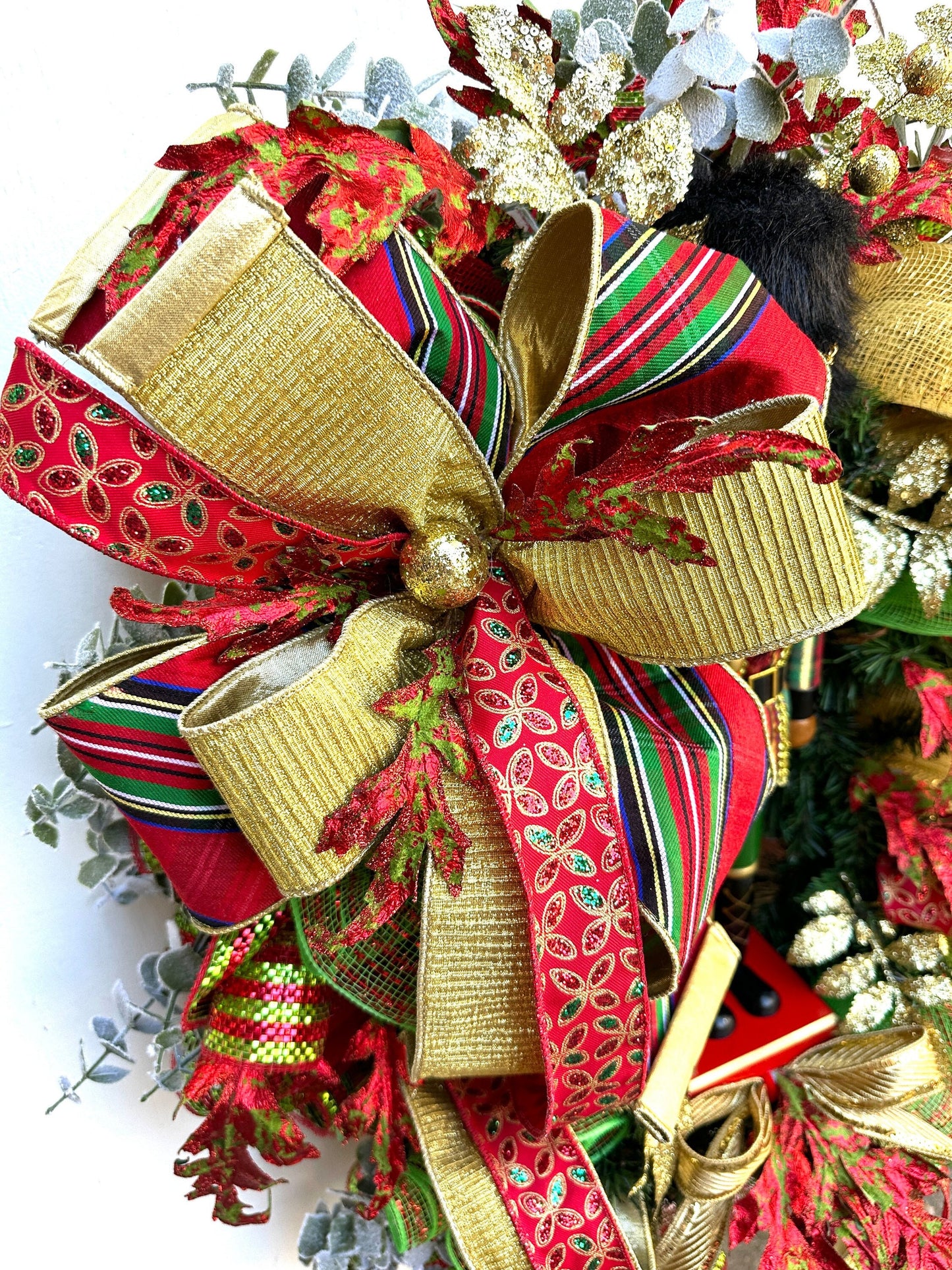 Christmas nutcracker red, green and gold nutcracker wreath features a dark face nutcracker soldier and a designer bow of 3 colorful ribbons.