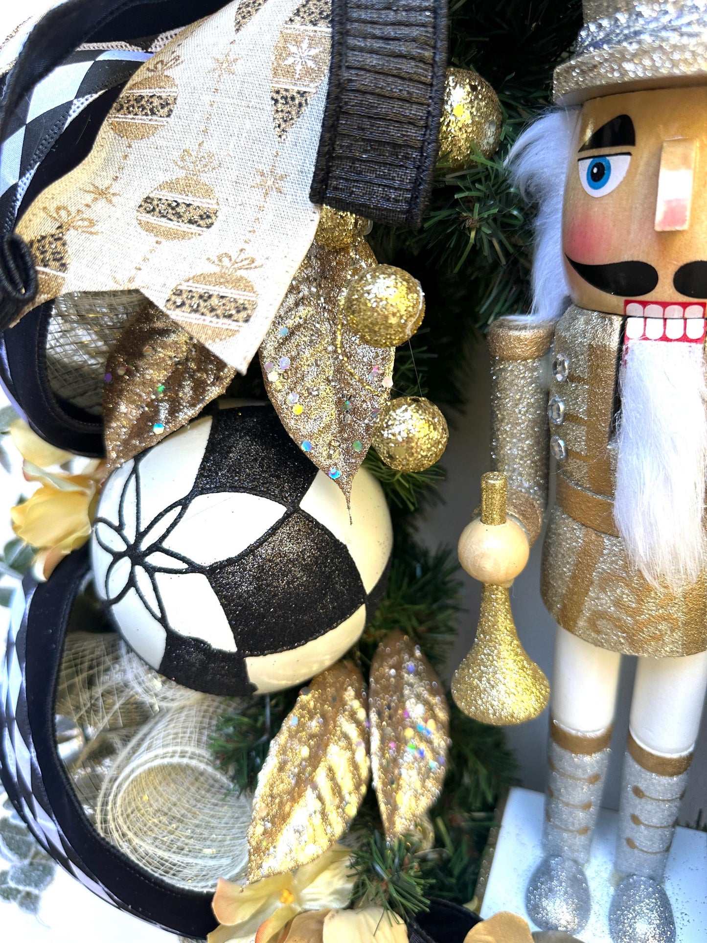 Nutcracker holiday front door Christmas wreath in gold and silver with designer ribbons featuring a wooden figure and black harlequin ribbon