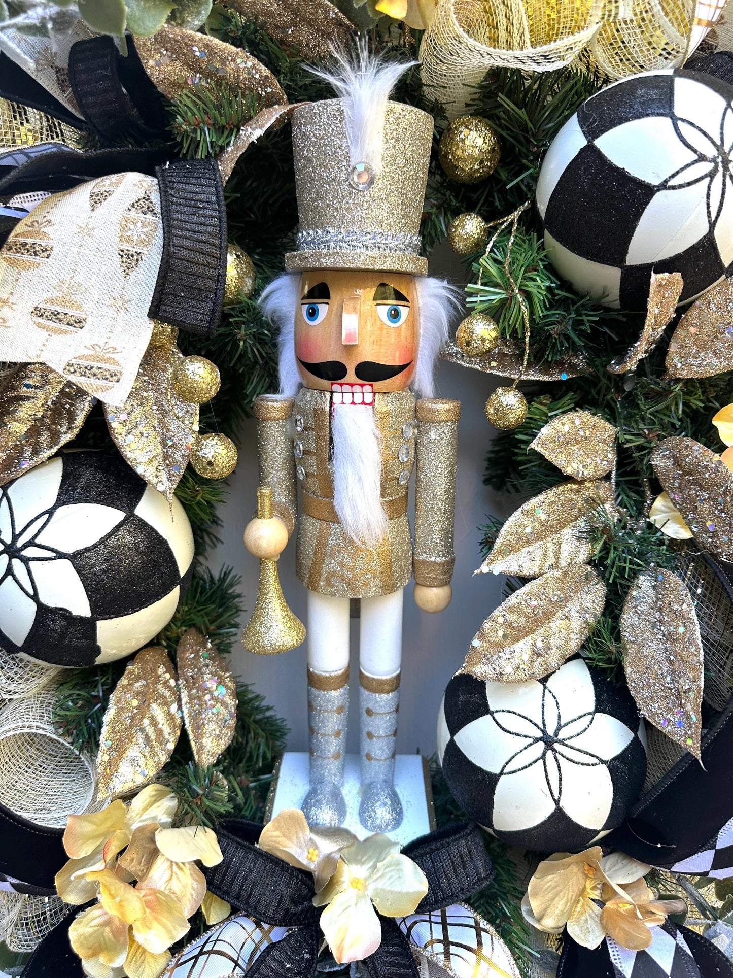 Nutcracker holiday front door Christmas wreath in gold and silver with designer ribbons featuring a wooden figure and black harlequin ribbon