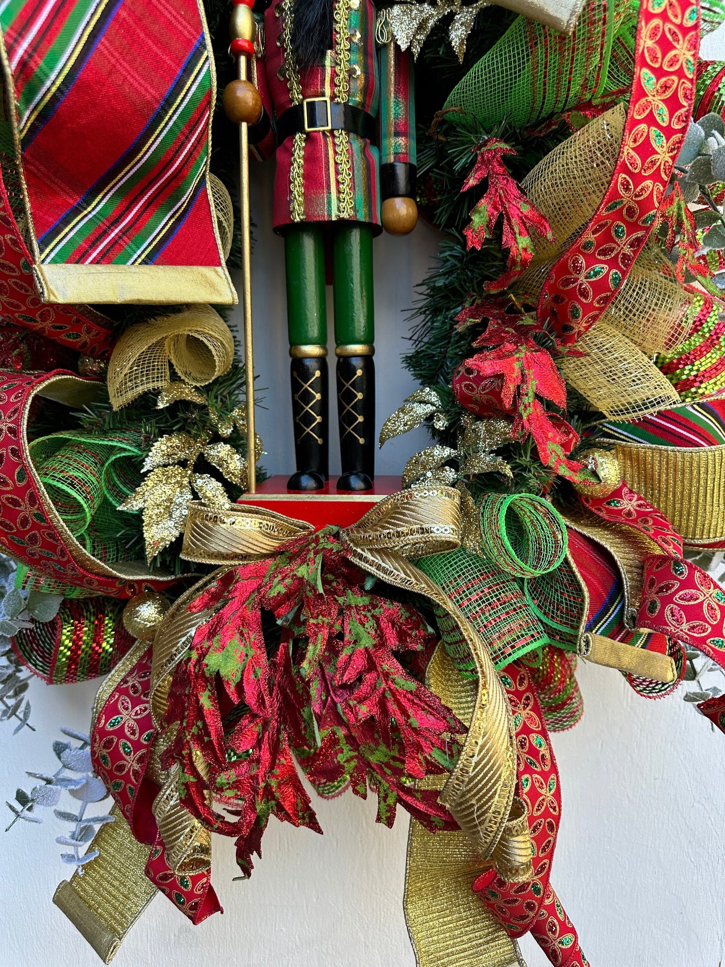 Christmas nutcracker red, green and gold nutcracker wreath features a dark face nutcracker soldier and a designer bow of 3 colorful ribbons.