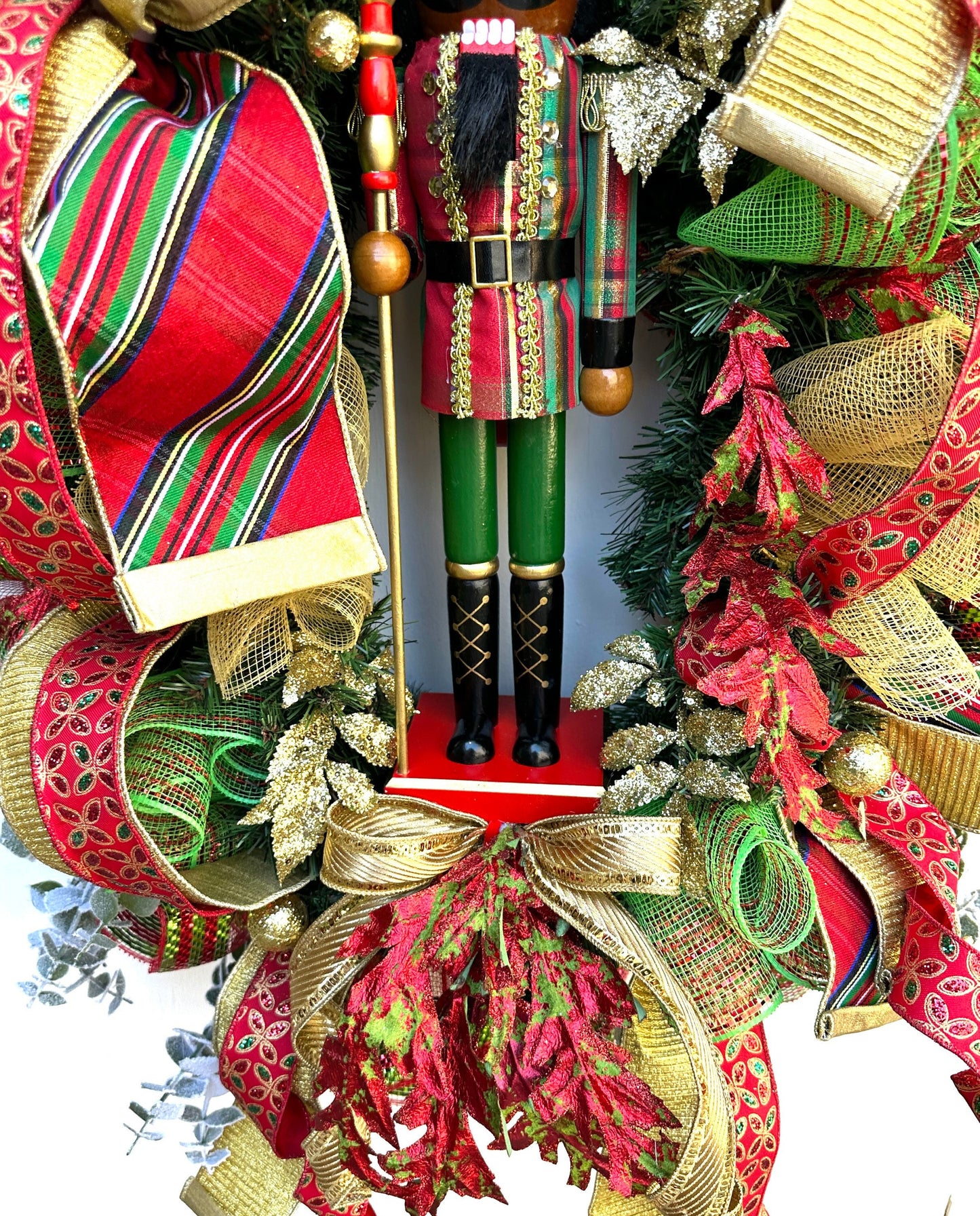 Christmas nutcracker red, green and gold nutcracker wreath features a dark face nutcracker soldier and a designer bow of 3 colorful ribbons.
