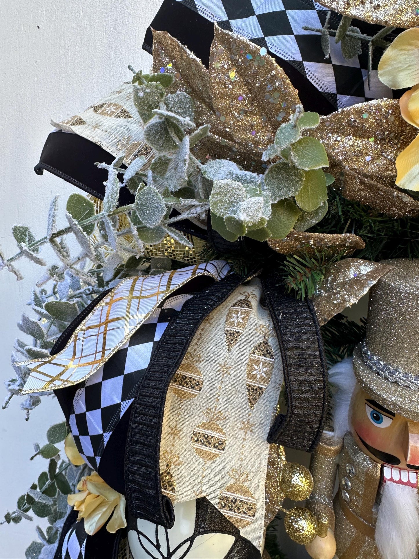 Nutcracker holiday front door Christmas wreath in gold and silver with designer ribbons featuring a wooden figure and black harlequin ribbon