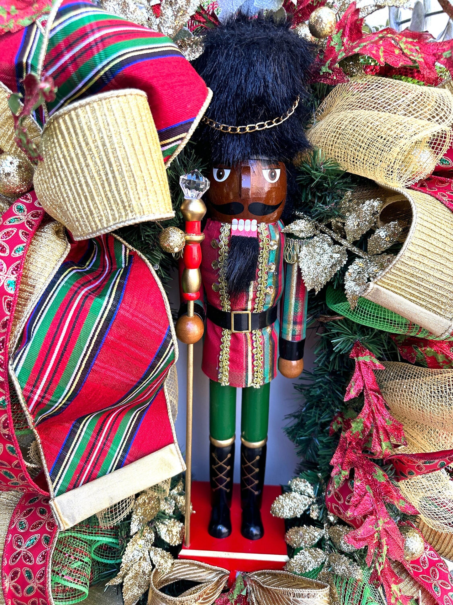 Christmas nutcracker red, green and gold nutcracker wreath features a dark face nutcracker soldier and a designer bow of 3 colorful ribbons.