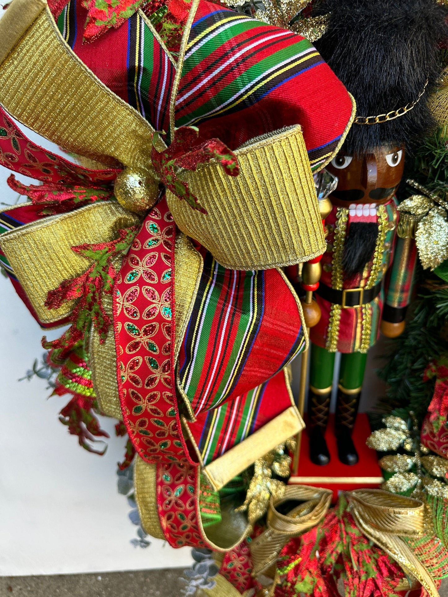 Christmas nutcracker red, green and gold nutcracker wreath features a dark face nutcracker soldier and a designer bow of 3 colorful ribbons.