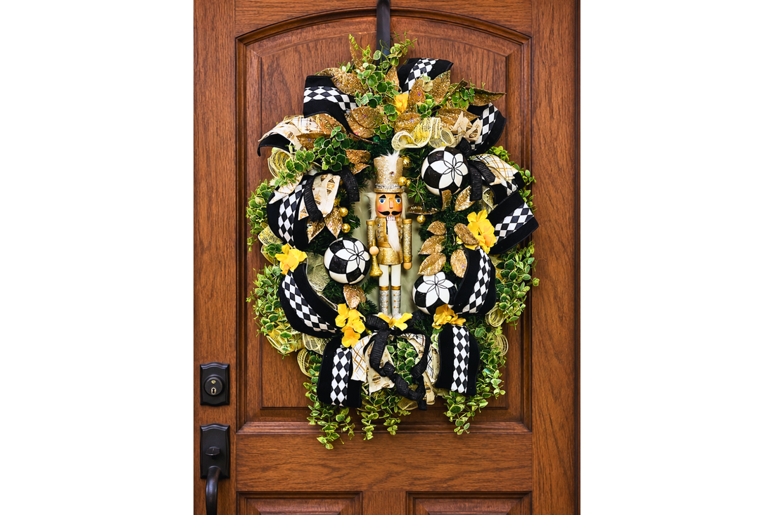 Christmas nutcracker themed wreath featuring a gold and white nutcracker figure, black and white harlequin ribbon, gold leaves, greenery and ornaments.