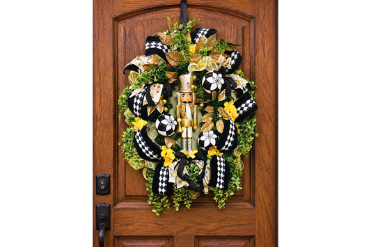 Christmas nutcracker themed wreath featuring a gold and white nutcracker figure, black and white harlequin ribbon, gold leaves, greenery and ornaments.
