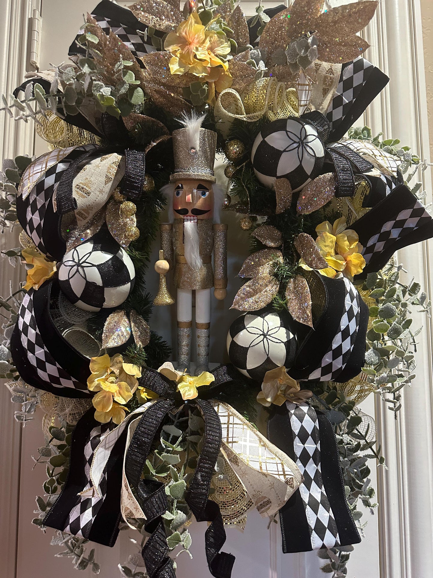 Nutcracker holiday front door Christmas wreath in gold and silver with designer ribbons featuring a wooden figure and black harlequin ribbon