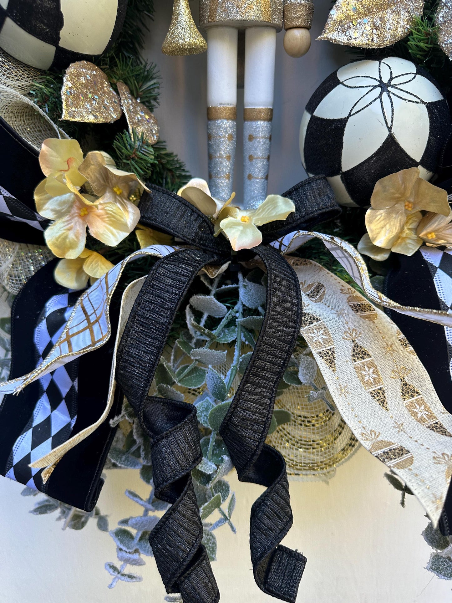 Nutcracker holiday front door Christmas wreath in gold and silver with designer ribbons featuring a wooden figure and black harlequin ribbon