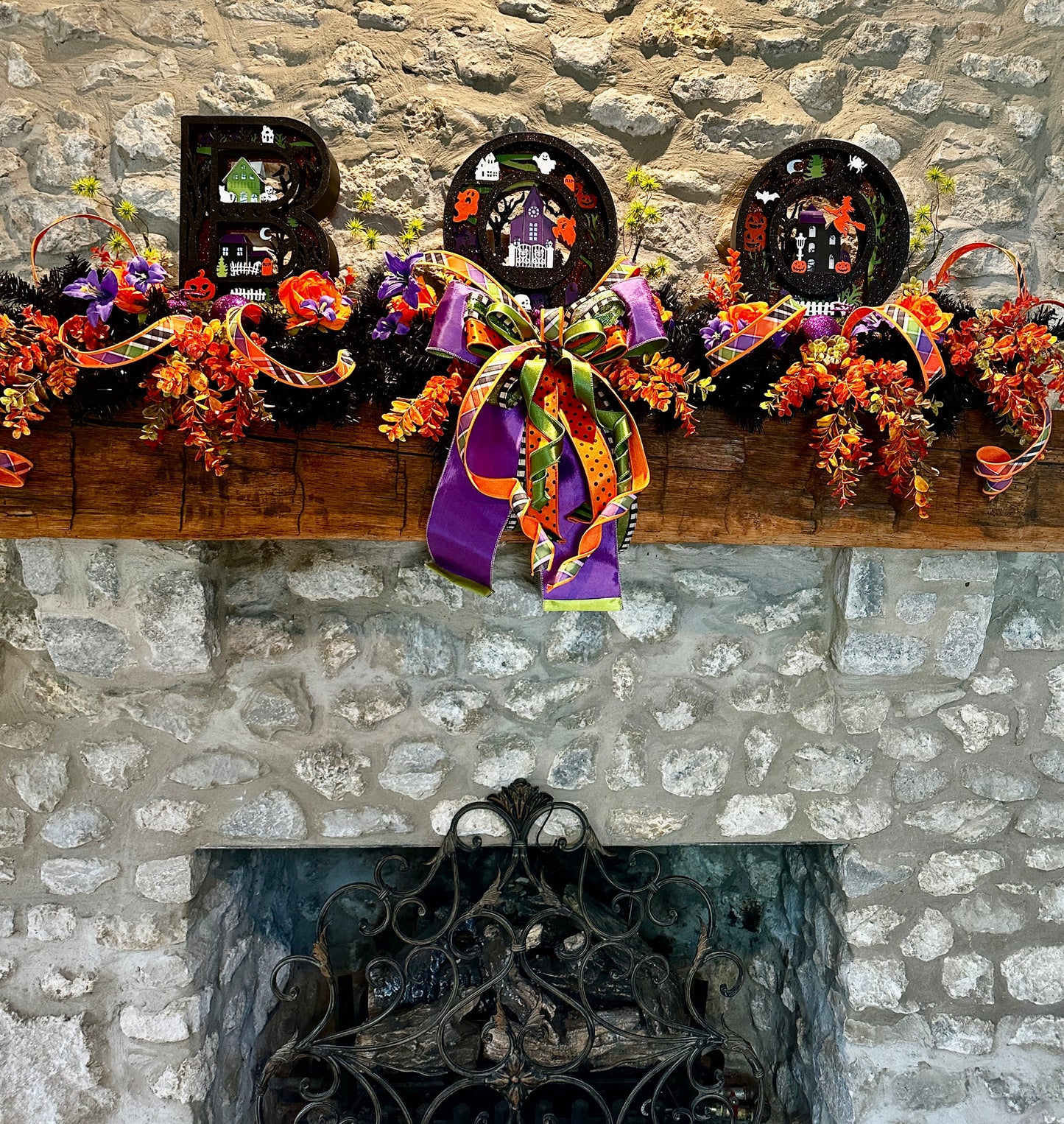 Decorative Halloween mantel with wreaths, ribbons, and 'BOO' letters against a stone fireplace.