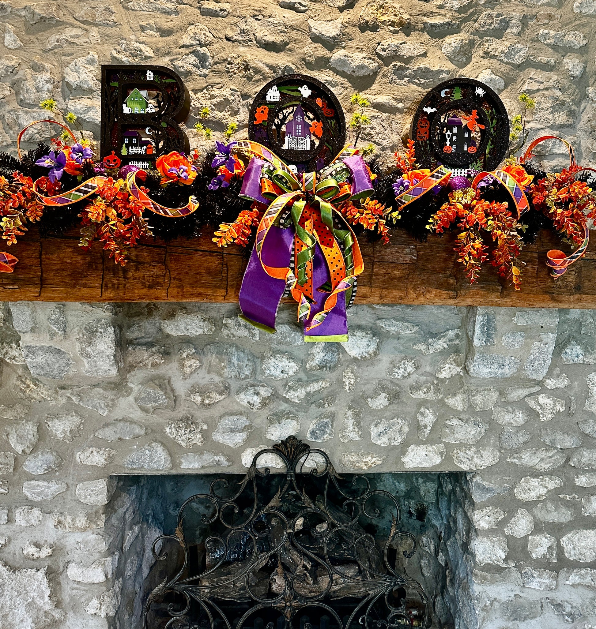 Decorative Halloween mantel with wreaths, ribbons, and 'BOO' letters against a stone fireplace.