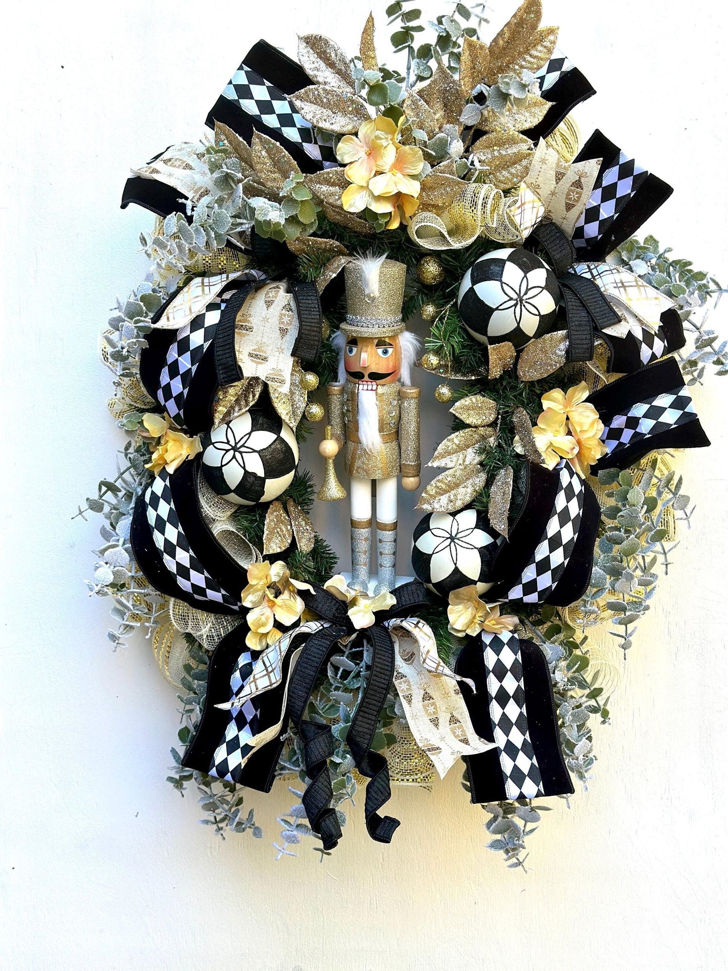 Nutcracker holiday front door Christmas wreath in gold and silver with designer ribbons featuring a wooden figure and black harlequin ribbon